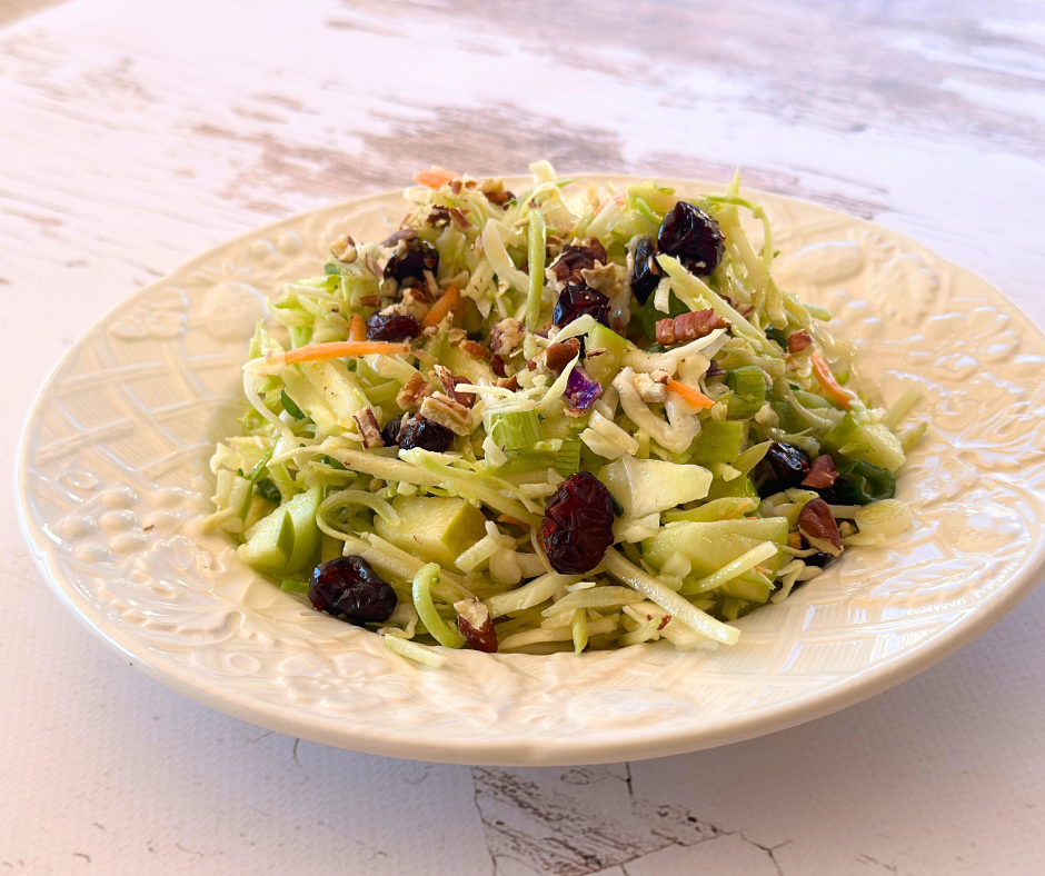 A fresh and colorful Sweet & Tangy Apple Slaw served on a plate, garnished with cranberries and pecans, with a drizzle of apple cider dressing for the perfect balance of sweet and tangy flavors