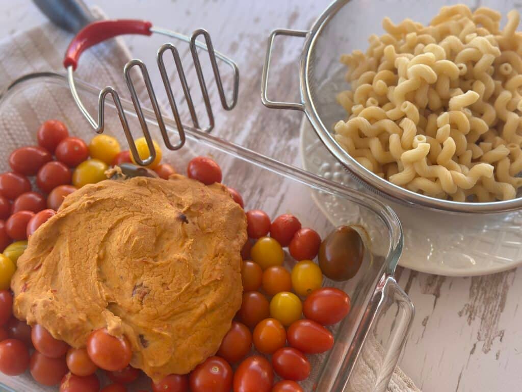 Baking dish filled with roasted tomatoes and hummus, ready to be mashed into a sauce.